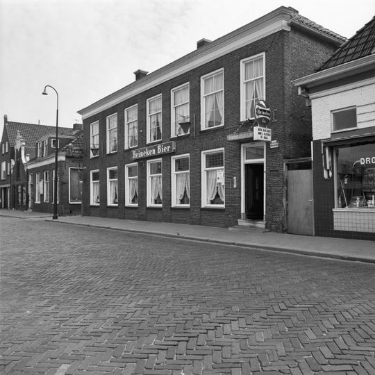 Zeven venstertraveeën breed pand met verdieping gedekt door laag schilddak met hoekschoorstenen waarop borden