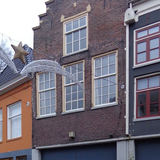 Pand met door halfrond fronton gedekte bakstenen trapgevel met sierankers en jongere onderpui