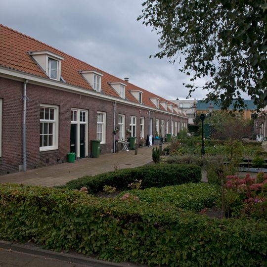 Dubbele rij van vierentwintig rug-aan-rug gebouwde woningen op rechthoekige plattegrond, bestaande uit een bouwlaag onder een met pannen gedekt mansardedak