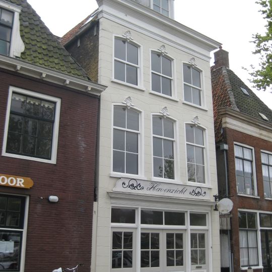 Hoog pand met gepleisterde gevel en rechte kroonlijst onder voor en achter afgeschuind zadeldak