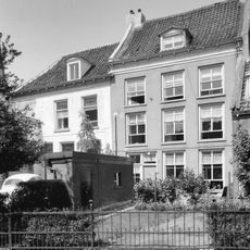 Door een diep erf van de straat gescheiden pand met half schilddak en gepleisterde lijstgevel