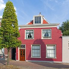 Pand met hoog, aan de voorzijde afgewolfd zadeldak en gewitte, ingezwenkte gevel onder getande lijst