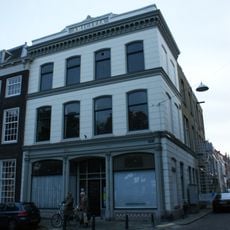 Hoekpand met statige lijstgevel in late Empire vormen. Rijk gesneden kroonlijst. De gevel is gepleisterd