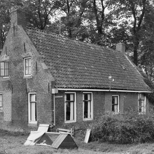 Eenvoudig huis aan de voet van het kerkhof onder zadeldak tussen topgevels met beitelingen en topschoorstenen