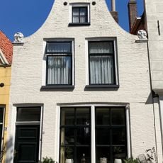 Pand onder zadeldak tegen klokgevel met aanzetkrullen en bekronende verhoogde lijst