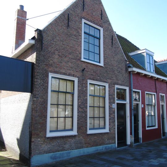 Pand met zadeldak, haaks op de straatas. Aan de voorzijde een puntgevel met vlechtingen. Vensters met twaalfruitsschuiframen