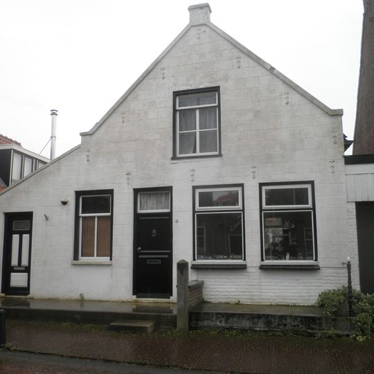 Woning met gepleisterde puntgevel onder zadeldak waarvan het linker schild dieper doorloopt dan het rechter