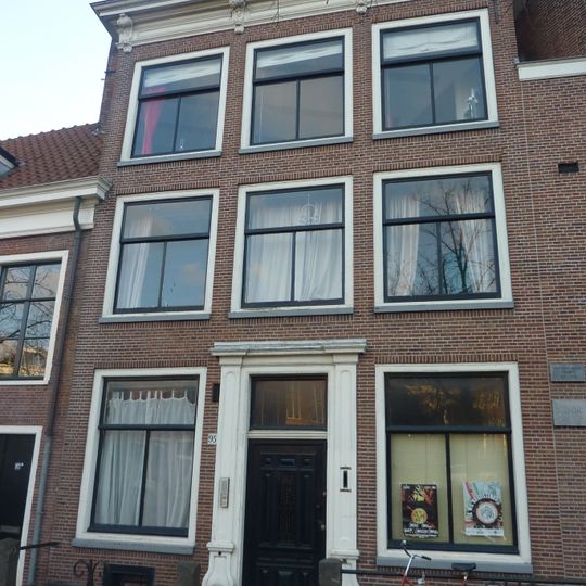 Pand met bakstenen gevel met rechte kroonlijst en gesneden consoles. Hardstenen stoep met palen. Deuromlijsting régence