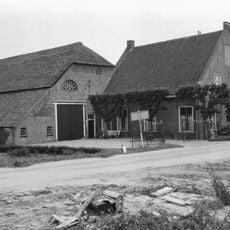 Grote hoeve, waarvan het woongedeelte een puntgevel met rollaag heeft. Geprofileerde zijdekplaten en in de top een jaartal. In de voorgevel vensters met zesruitsschuiframen.