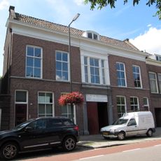 Breed koopmanshuis van parterre en verdieping met brede middenrisaliet, waarin hardstenen poortomlijsting met gebeeldhouwd opschrift "Noord-Holland" en jaartal