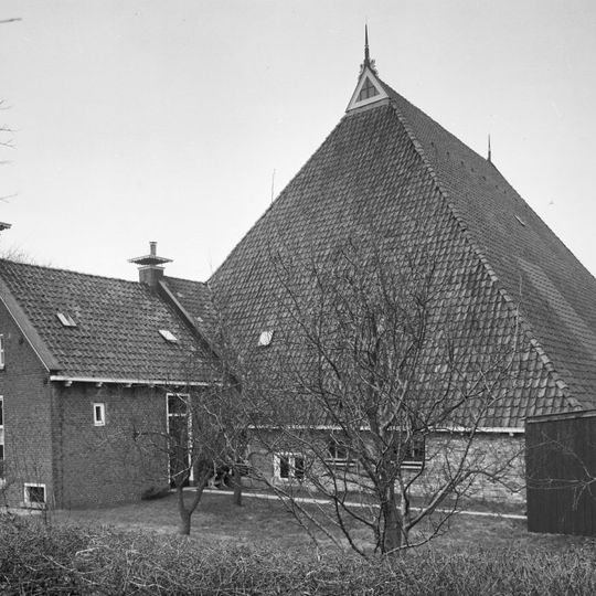 Eenvoudige kop-romp-boerderij met zeer hoge schuur en woondeel met houten deklijst en versierde schoorsteenborden