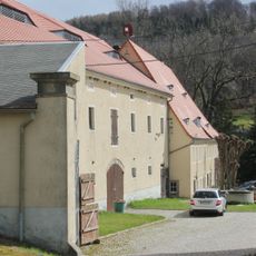 Südöstliches Wohnhaus über winkligem Grundriss mit angebautem Seitengebäude, nördliches Seitengebäude und westliche Scheune sowie nördliche Toreinfahrt mit zwei Torpfeilern, zwei Granittröge und Einfriedungsmauer an der Hauptstraße