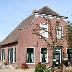 Boerderij. Voorgevel met ingezwenkte zijkanten en houten kroonlijst. Deuromlijsting met pilasters en hoofdgestel