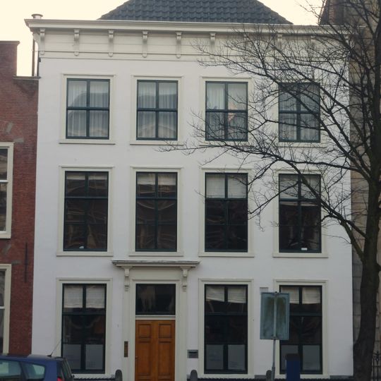 Pand met gepleisterde lijstgevel. Stoep met hardstenen palen met ijzers