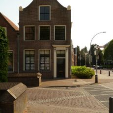 Pand met gaaf bewaarde, bakstenen topgevel met ingezwenkte zijkanten, gebeeldhouwd fronton met schelpversiering en natuurstenen hoekvoluten