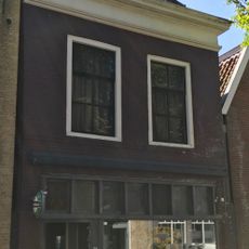 Pand onder diep zadeldak met voorschild en schoorsteen met bord