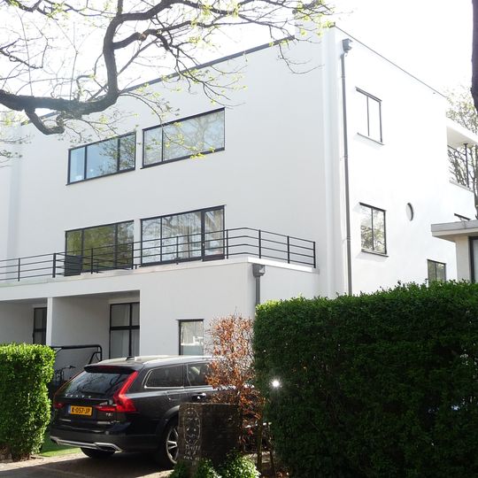 Vrijstaand, in baksteen opgetrokken, witgepleisterd, rechtafgesloten, vlakgedekt blok van twee woonhuizen