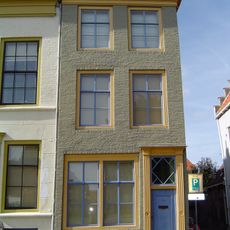 Huis met geverfde lijstgevel. Kroonlijst voorzien van drie tandlijstjes. Dakkapel met tandlijstje. Eenvoudige voordeuromlijsting met bovenlicht en kalf met twee tandlijstjes. Stoeptreden