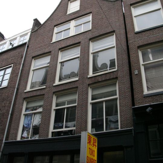 Uitwendig voornamelijk 19e-eeuws huis waarvan de gevel wordt bekroond door een klokvormige top onder rollagen en afsluitende lijst