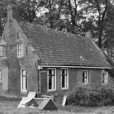Eenvoudig huis aan de voet van het kerkhof onder zadeldak tussen topgevels met beitelingen en topschoorstenen (voorm. kosterij en school)