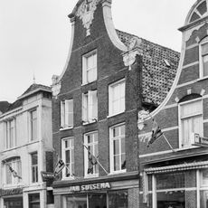 Pand met twee verdiepingen onder zadeldak tegen klokgevel met gebeeldhouwde aanzetkrullen, deklijst en bekroning met voorstelling van passer, driehoek en schietlood