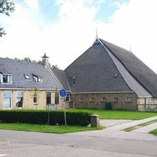 Kop-hals-rompboerderij met voorhuis met omgaande goot onder zadeldak tussen puntgevels met schoorstenen waarop borden