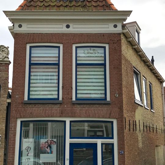 Hoekpandje met sober versierde rechte kroonlijst onder hoog schilddak met topschoorsteen