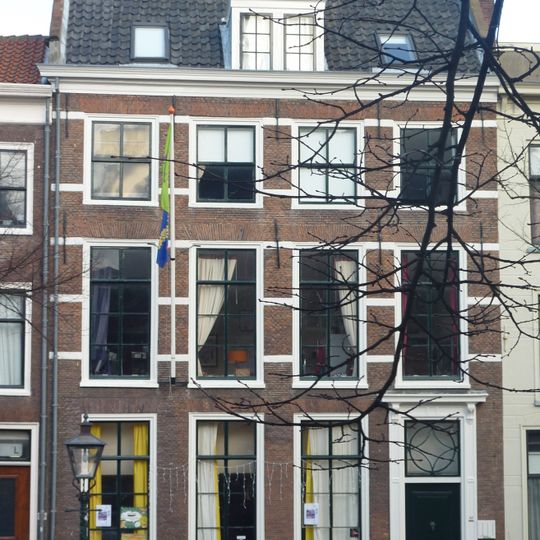 Pand met bakstenen gevel met rechte kroonlijst. Hardstenen stoep met palen. Speklagen, zadeldak in topgevels terzijde eindigend