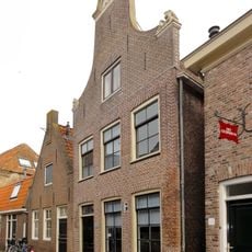 Huis met klokgevel met geveltop met natuurstenen aanzetvoluten en topstuk met jaartalcartouche en schelpversiering