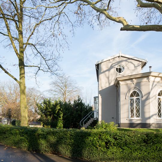 Gepleisterd 6-hoekig gebouwtje met spitsboogvensters, waarin authentieke ruitvormige roedeverdeling. Fijn gedetailleerde kroonlijst met consoles