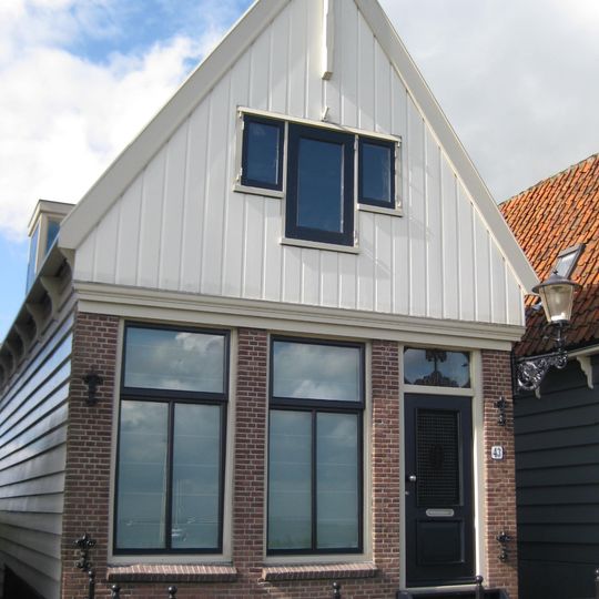 Houten huis. Voorschot in puntvorm, nog met voormalig luikkozijn met aangekoppelde vensters. Pui laatste helft 19e euew in baksteen vernieuwd