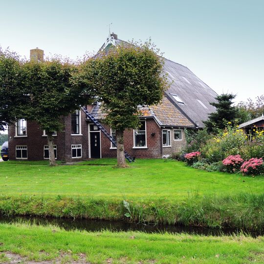 Kop-rompboerderij met onderkelderd voorhuis en houten beschieting met sierlijst boven de inrit van de schuur