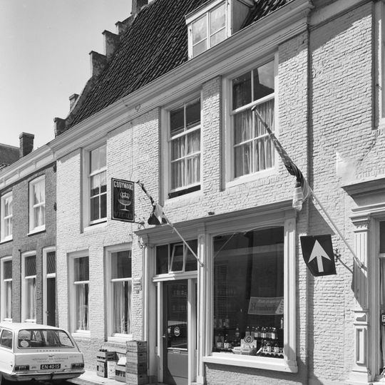 Onregelmatig pand waarvan de hoge kap aan de ene zijde aansluit tegen een verminkte zijtrapgevel met sierankers en aan de andere zijde is afgewolfd.