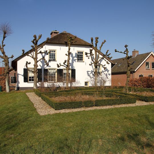 Gepleisterde boerderij met vormbomen ervoor. Brede gevel, afgewolfd dak, opkamer