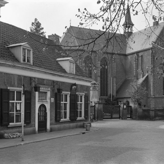 Laag dorpshuis in gele baksteen met zadeldak mede van belang door situatie naast kerk