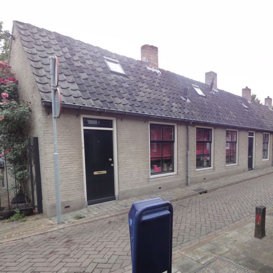 19e eeuws arbeiderswoninkje zonder verdieping onder met blauwe Hollandse pannen gedekt zadeldak, dat doorloopt over de buurpanden