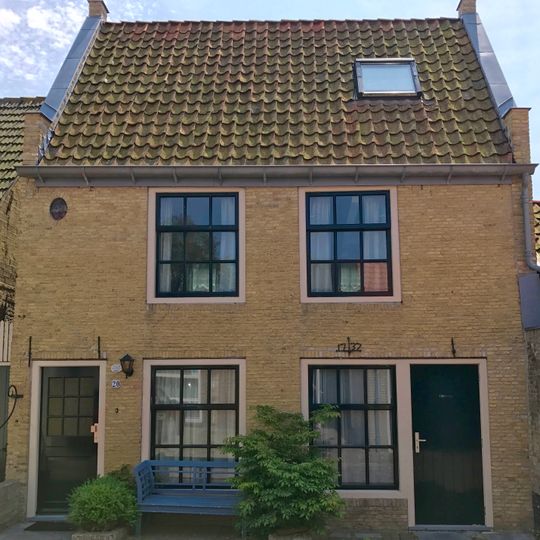 Hoog pand onder zadeldak tegen twee topgevels van gele steen