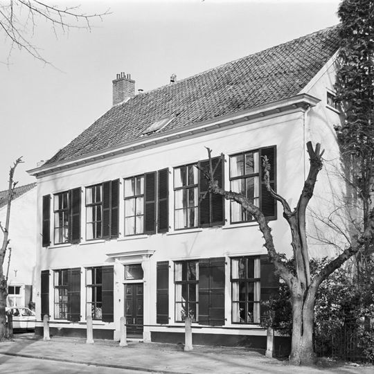 Huis met witgepleisterde lijstgevel, groene vensterluiken en ingang met kroonlijst op voluutvormige consoles