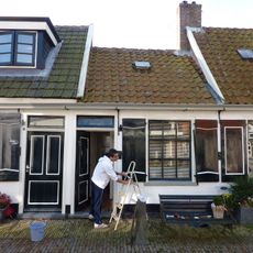 Klein huisje onder een dwars dak met de nummers 8 en 12. Aardige details aan vensters. Luiken en goede deur. Achterschot