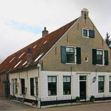 Pand met gepleisterde puntgevel, bekronend fronton en eenvoudige deuromlijsting