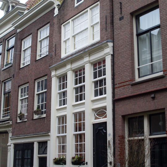 Huis achter gevel met hoge pui en klokvormige top onder rollagen en fronton