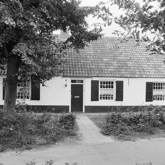 Grotendeels gepleisterde boerderij onder pannen wolfdak. Vensters met 25-ruitsschuiframen