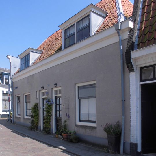 Pand met zolderverdieping en hoog schilddak, dat aan de voorzijde is afgewolfd boven de lijstgevel met getoogde deur en vensters