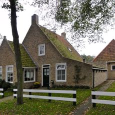 Pandje met zesruitsvensters onder zadeldak tegen topgevel met beitelingen en topvenster terzijde van het rookkanaal