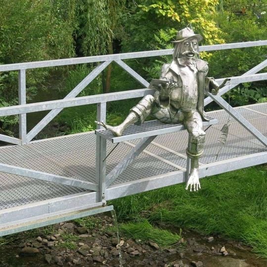 Kovová plastika vodníka na lávce přes potok Popelka v Nové Vsi nad Popelkou