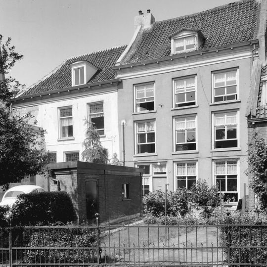 Door een diep erf van de straat gescheiden pand met half schilddak en gepleisterde lijstgevel