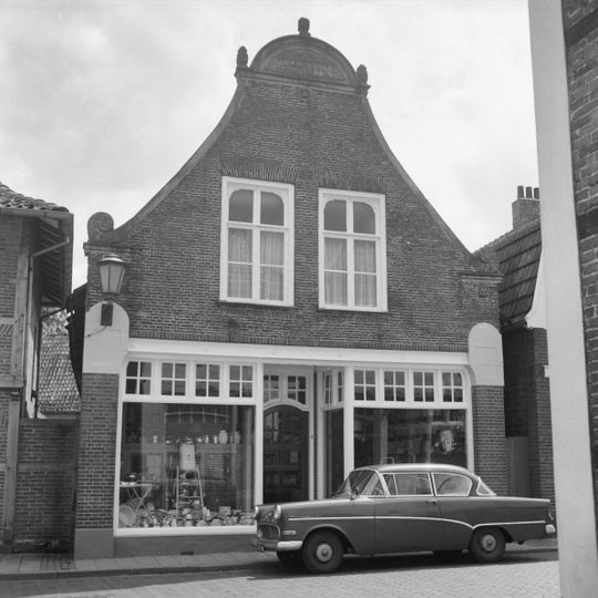 Pand met ingezwenkte halsgevel met zandstenen aanzetkrullen, lijsten en halfrond fronton. Onderpui gewijzigd