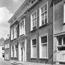 Fors L-vormig pand onder schilddak met gepleisterde rechte gevels. Kroonlijst met klossen