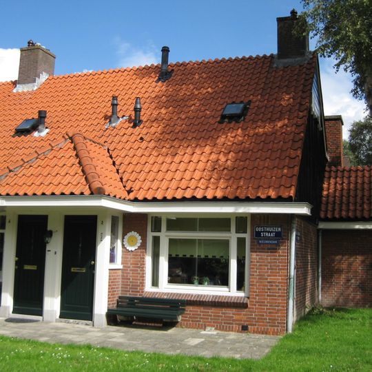 Blok met 9 woningen, gecombineerde toegangen van twee woningen onder een ingestoken schilddak, zijkant met houten topgevel, onderdeel van complex bejaardenwoningen in Tuindorp Nieuwendam