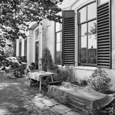 Gebouw op T-vormige plattegrond onder schilddaken met op het dwarshuis hoekschoorstenen met borden